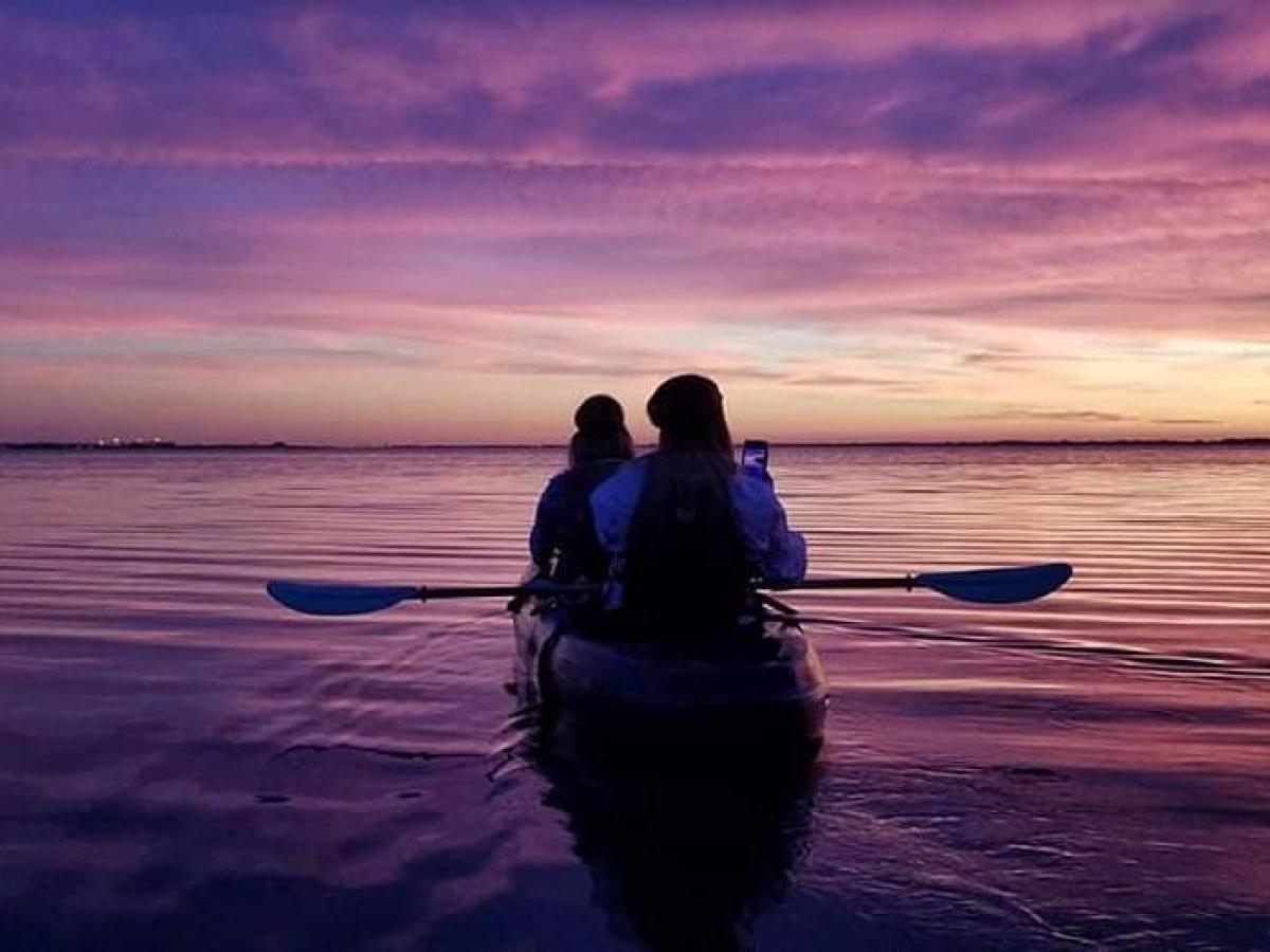 a person standing in front of a sunset over a body of water