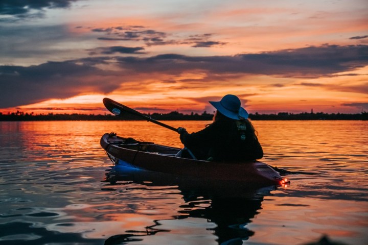 a small boat in a body of water with a sunset in the background