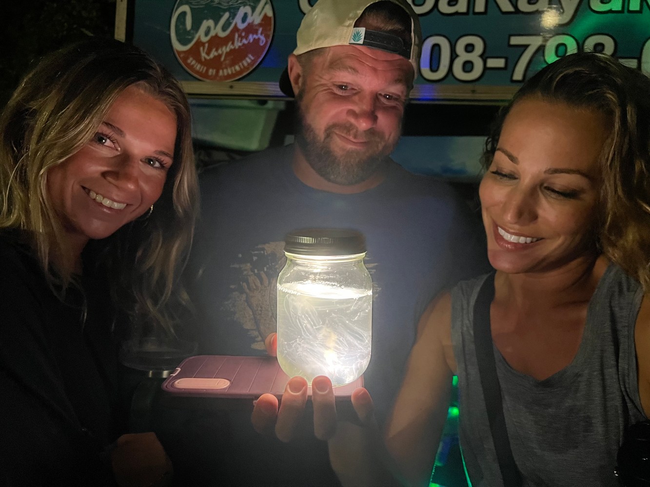 Three people smiling, holding a glowing jar in the dark.