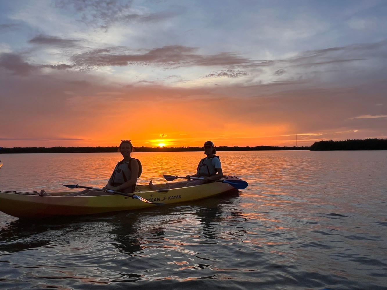 Two people kayaking on a lake during a sunset with vibrant sky.