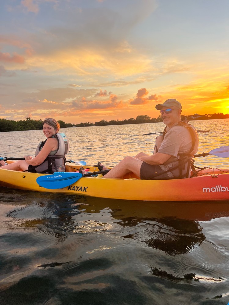 Two people kayaking at sunset on a calm lake with colorful sky.
