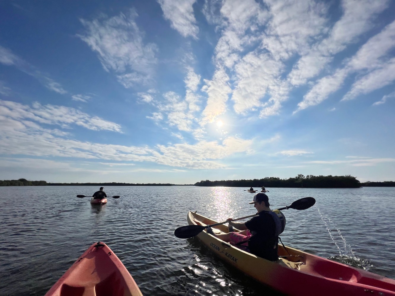 People kayaking on a sunny lake with a blue sky and scattered clouds.