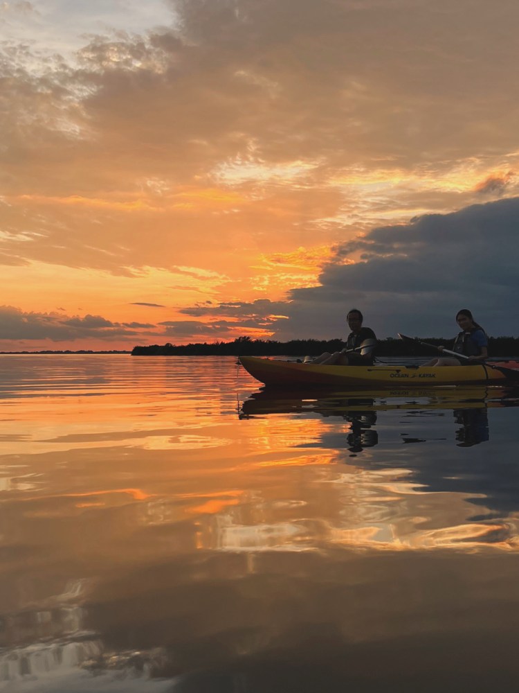 Two people kayaking on calm water during a vibrant sunset.