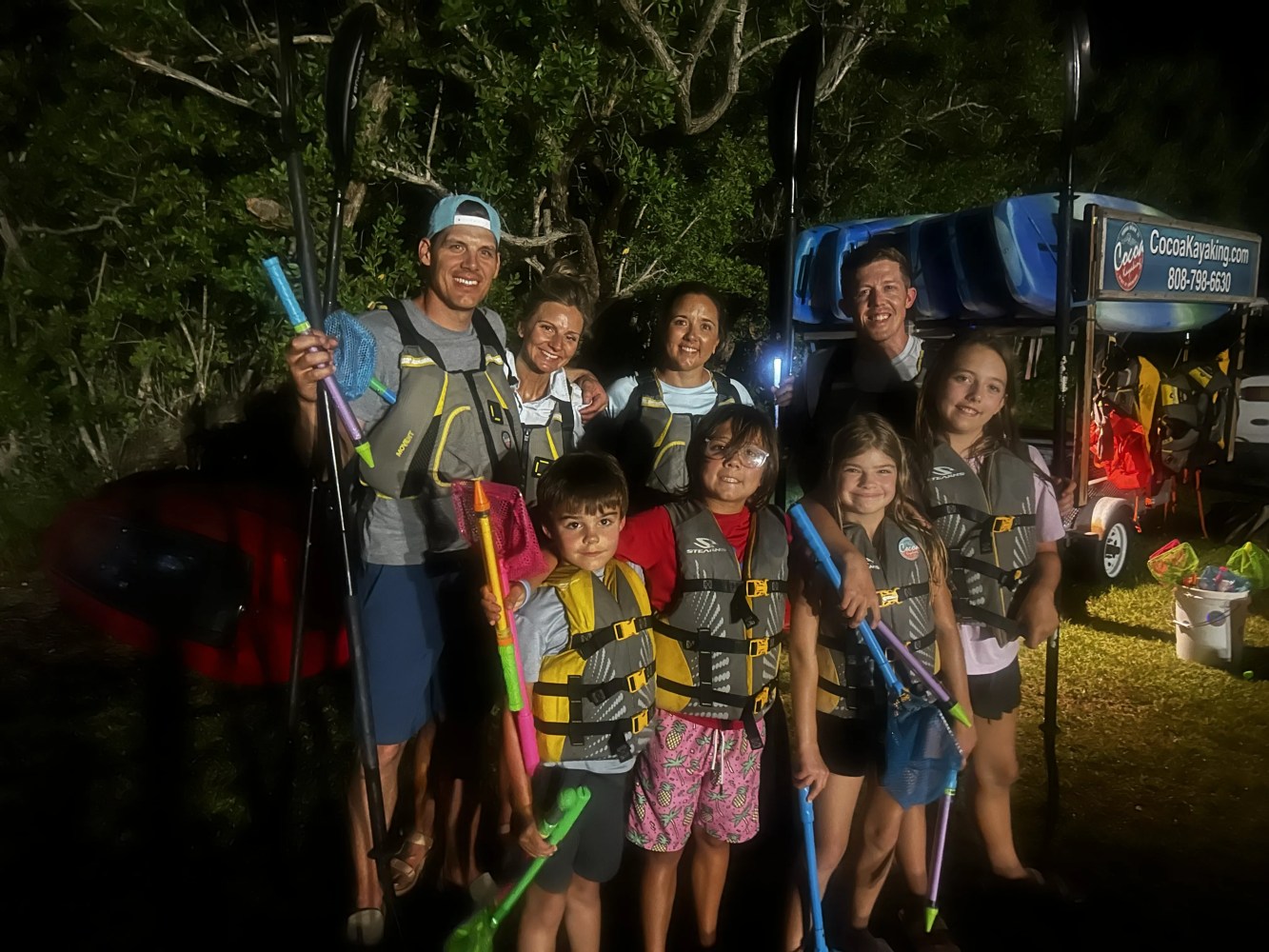 Group of adults and children posing with kayaking gear at night.