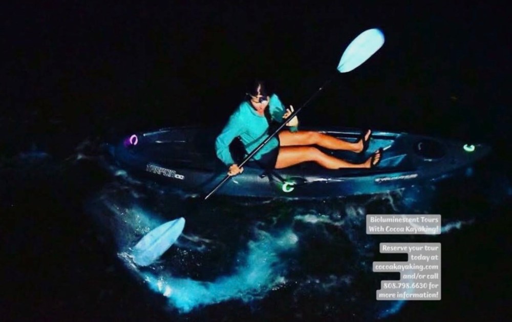 Person kayaking at night with visible bioluminescent water.