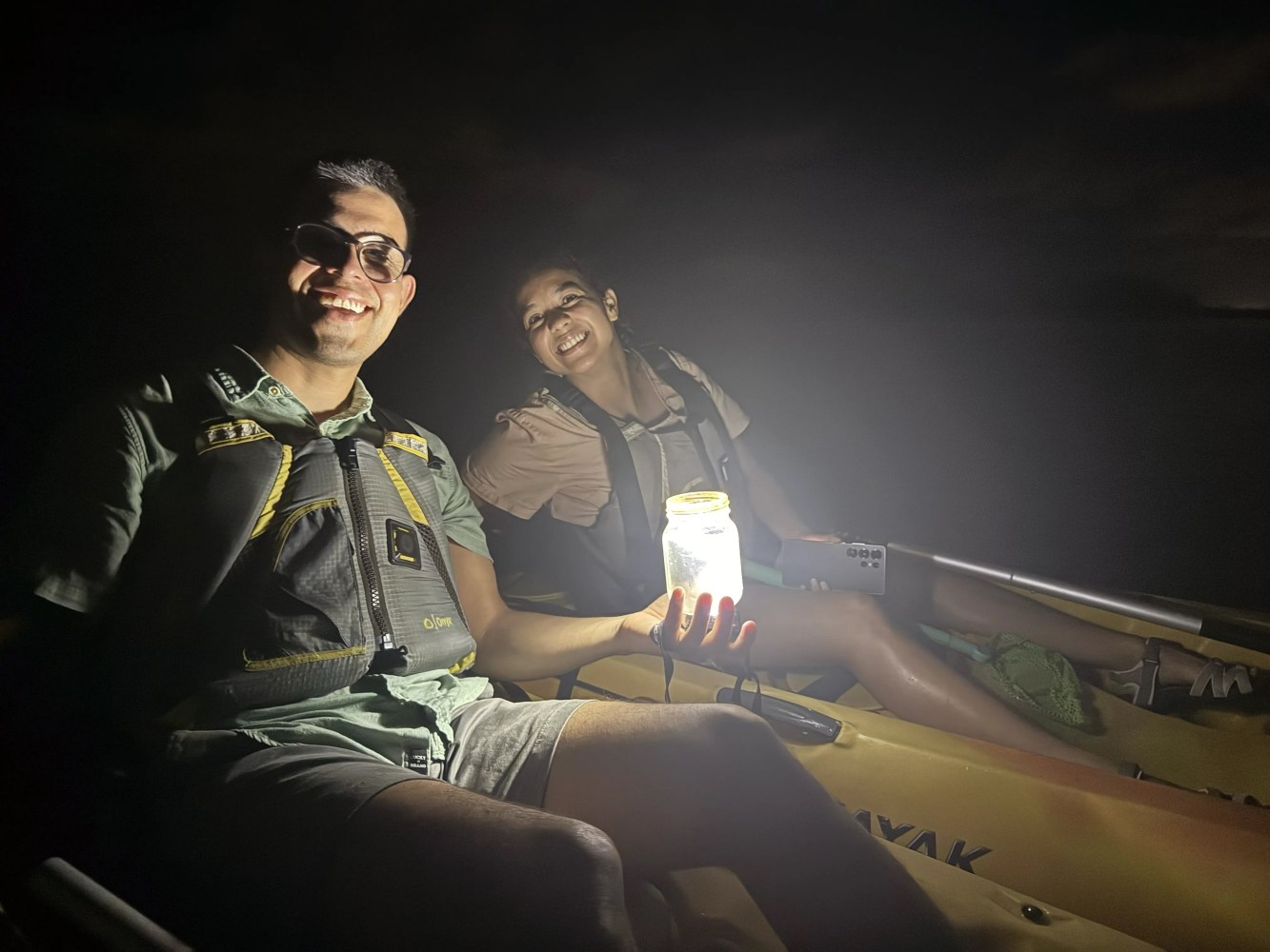 Two people in a kayak at night, one holding a glowing jar.